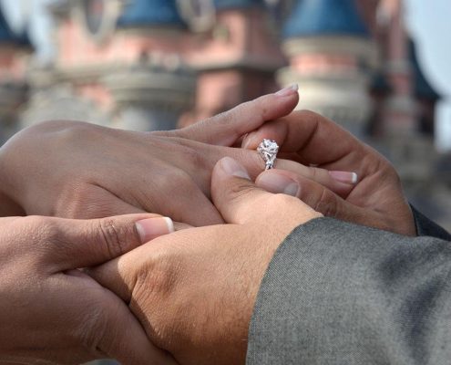 Groom putting engagement ring on bride fingers with EuroDisney backdrop